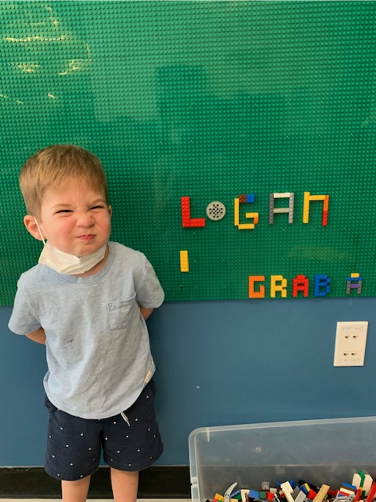 A child standing in front of a green board with colorful blocks Description automatically generated